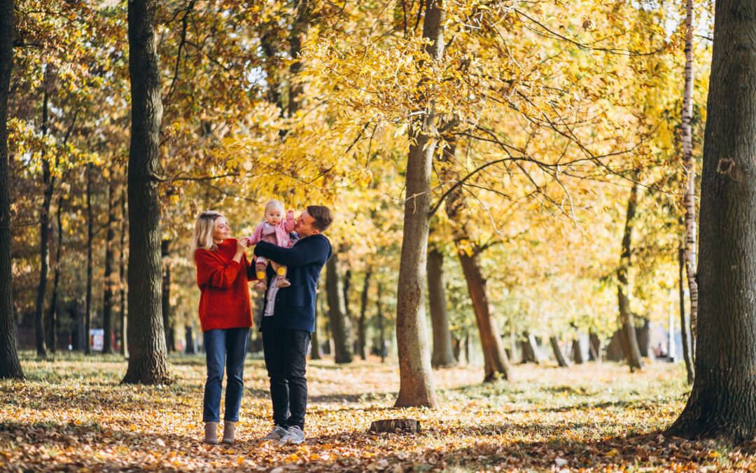 Eltern gehen mit einem Baby durch einen Park mit Herbstlaub